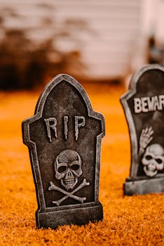 Decorative gravestones with inscription placed in yard on ground with dry grass near white building on blurred background during holiday celebration